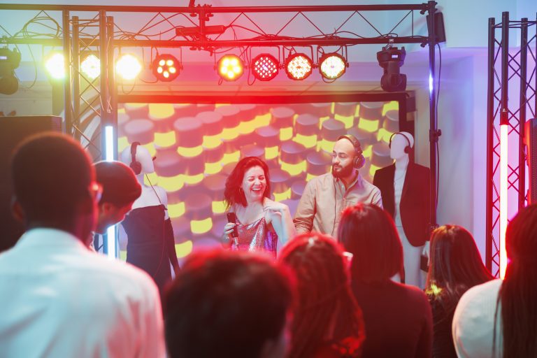 Singer and dj band performing on stage while crowd clubbing at dance party in club. People having fun on dancefloor while musicians playing at electronic music festival in nightclub